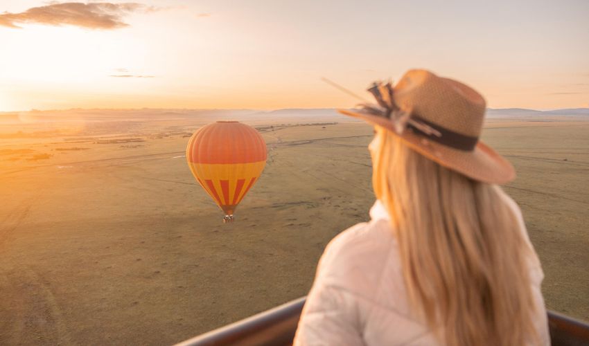 Traveler in a safari hat enjoying a sunrise hot air balloon ride over the Maasai Mara in Kenya.