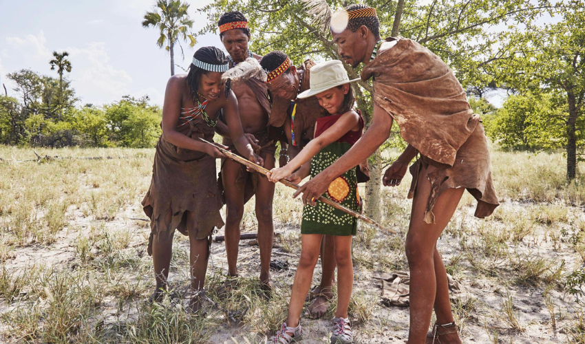 Local San guides teaching a young traveller traditional bushcraft skills during a cultural experience near Jack’s Camp in Botswana.